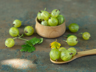 Ripe green gooseberries in a wooden bowl and spoon on an old iron background. Vegetarian food.