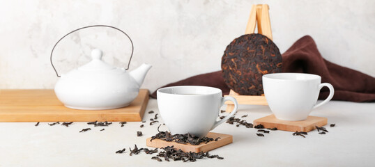Cups of tasty puer tea and teapot on light table