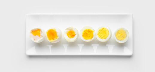 Different stages of boiling eggs on white background, top view