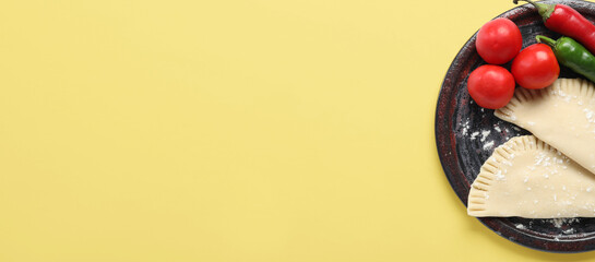 Plate with raw chebureks, tomatoes and chili peppers on yellow background with space for text, top view