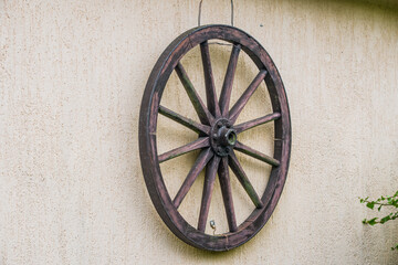 Historic wooden wheel hanging on the wall with a metal hub and a metal rim outside