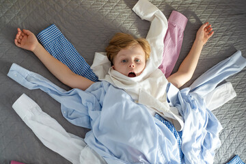A boy in a pile of clothes on a bed. top view. Recycling of clothes. Ecological and sustainable...