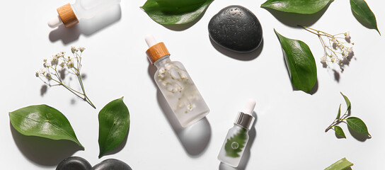 Composition with bottles of cosmetic serum, spa stones, plant leaves and flowers on white background
