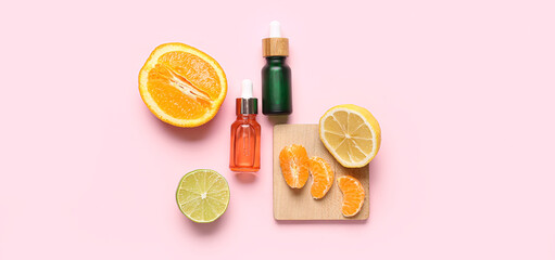 Bottles of citrus essential oil and fruits on pink background, top view