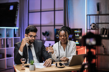 Multi ethnic financiers coworkers, attractive confident arab bearded office manager and african businesswoman recording video vlog for internet audience in evening office.