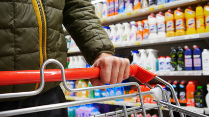 Close-up of a male buyers hand pushing a shopping cart in a household chemicals department