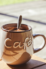 A large brown ceramic coffee mug on a wooden table on the terrace on a sunny summer day, relaxing on the terrace on a sunny summer day, relaxed, cozy atmosphere. hedonic holidays. Place for your text