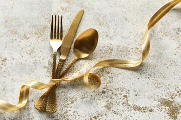 Golden cutlery with ribbon on grunge background