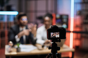 View from screen of camera with diverse colleagues, smiling successful african american businesswoman and indian it specialist in formal wear recording new video for their internet business course.