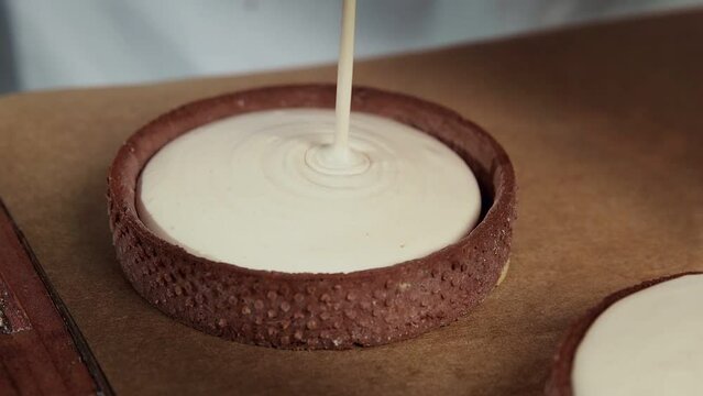 Chef adding white cream to the small tarts with chokolate