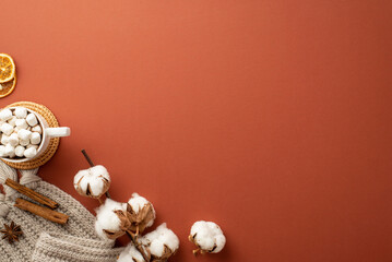 Winter concept. Top view photo of knitted blanket mug of hot drinking with marshmallow rattan serving mat dried orange slices cinnamon sticks cotton branch on isolated brown background with copyspace