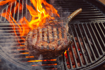 Barbecue dry aged wagyu tomahawk steak offered as close-up on a charcoal grill with fire and smoke