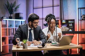 Overjoyed multiracial business people, african american businesswoman and indian broker getting good news in evening office looking at laptop screen.