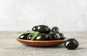 Plate with tasty black olives on table
