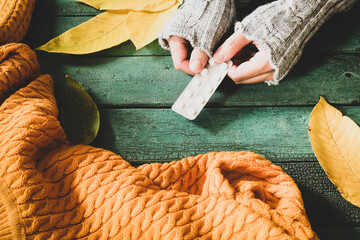 Woman hands wearing cozy warm knitted sweater holding a blister of pills as autumn flu treatment
