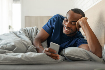 Black Guy Texting On Cellphone Browsing Internet Lying In Bedroom