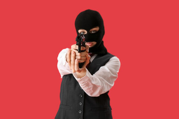 Young woman in balaclava aiming gun against red background