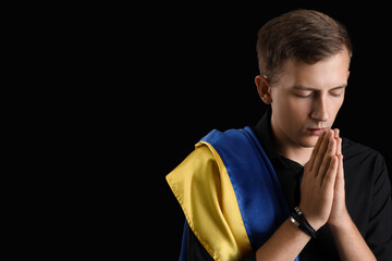 Young man with flag of Ukraine praying on black background