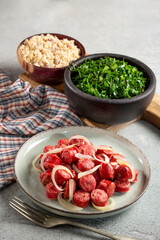 Sliced sausage with onion, green cabbage and farofa.