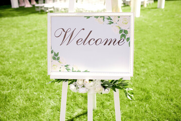 A white board with the inscription welcome stands on a green lawn. Signboard with the invitation of...