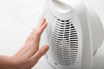 Woman warming near electric fan heater at home, closeup