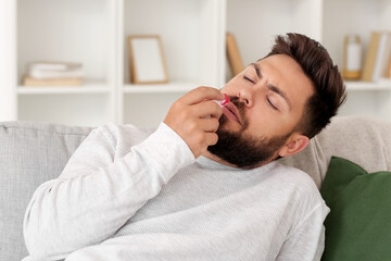 Young bearded man with nosebleed and tissue at home
