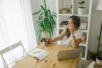 Portrait of cheerful adult businesswoman working from home, she is hawing a break and drinking coffee