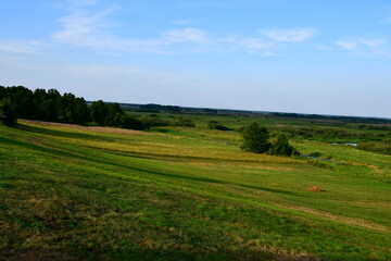 Fototapeta premium A view from the top of a tall hill with numerous trees, shrubs, and forest formations visible next to some fields, meadows, and pasturelands spotted on Polish countryside in summer