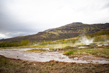 Fototapeta na wymiar Icelandic geyser with mountain in the background on an overcast day during the summer