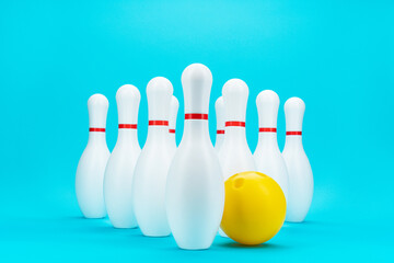 Minimalist photo of bowling pins over turquoise blue background. Image of white bowling pins and yellow bowling ball central composition.