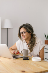 Smiling woman having online meeting at home via laptop