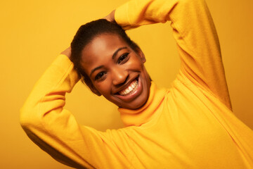 Attractive African American woman in a yellow sweater smiles happily with her arms crossed behind her head.