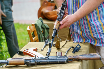 A man in a shirt is holding a loaded Kalashnikov assault rifle. Exhibition of weapons for the...