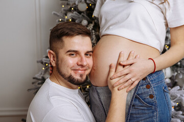 A man and his pregnant wife pose against the background of a Christmas tree