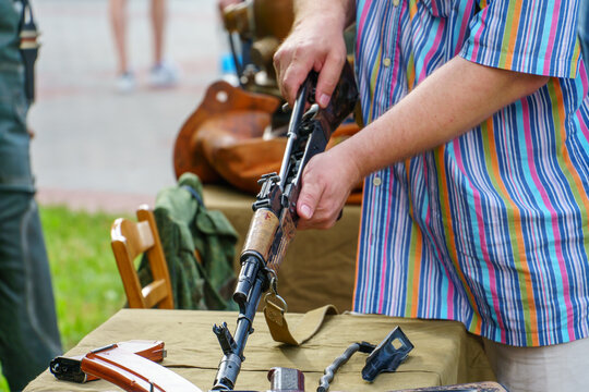 A man in a shirt is holding a loaded Kalashnikov assault rifle. Exhibition of weapons for the Russian army. A military man with a gun in his hands.