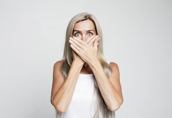 Portrait of beautiful nice shocked gray-haired old woman covering her mouth with palms.