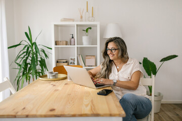 Happy woman texting on social media via laptop at home