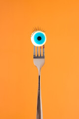 Blue Halloween eyeball candie impaled on a fork tines against vivid orange background. Spooky...