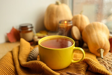 Cup of hot tea, sweater, candle and pumpkins on the windowsill, autumn atmosphere