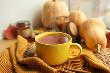 Cup of hot tea, sweater, candle and pumpkins on the windowsill, autumn atmosphere
