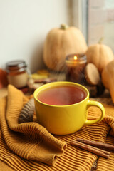 Cup of hot tea, sweater, candle and pumpkins on the windowsill, autumn atmosphere