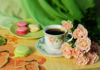 Fototapeta na wymiar A cup of coffee, macaroons, and a bouquet of pink roses on a green chiffon background, a horizontal holiday composition with sweets for a greeting card, poster, etc.