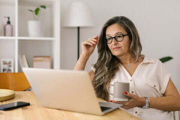 Woman holding cup of coffee and looking at the computer