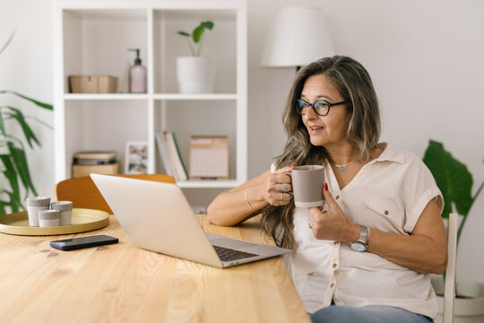 Woman Holding Cup Of Coffee And Looking At The Computer