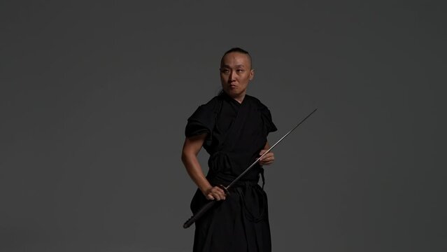 Japanese man traditional dress, black kimano katana samurai sword strikes, takes out scabbard, holds handle, trains kenjutsu, practices techniques, sword training combat principles samurai fighting