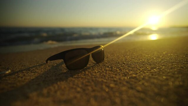 Sunglass on the beach sand at sunset. Waves floating on the sand and golden sun in the sky background