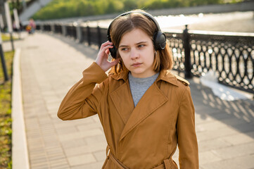 Young teenage girl listens to music in headphones, walks along the embankment in the city. High quality photo