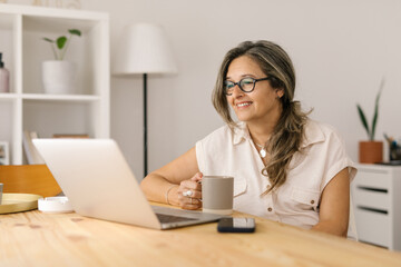 Woman holding a cup and reading from computer screen