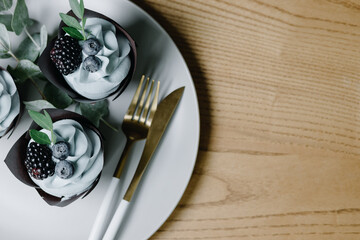  Three chocolate cupcakes with berries on a white plate with a fork on a knife. View from above.