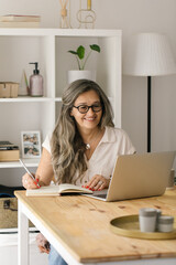 Mature happy female taking notes from online meeting